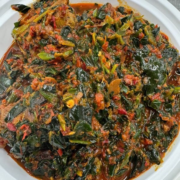 A close-up of a Nigerian dish with dark green leafy vegetables and red sauce in a white bowl.