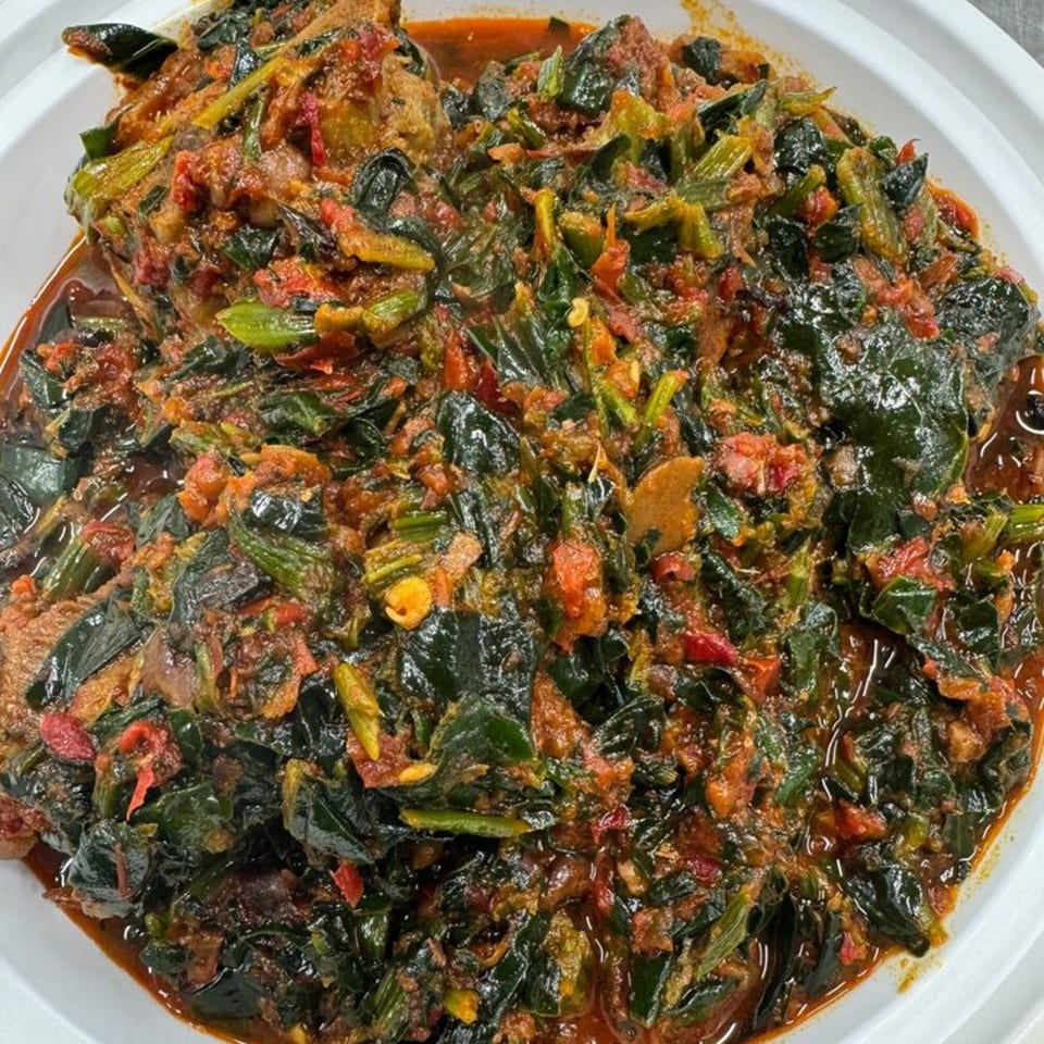 A close-up of a Nigerian dish with dark green leafy vegetables and red sauce in a white bowl.