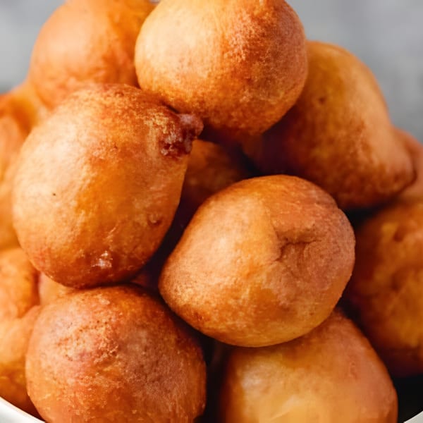 A close-up of a pile of golden-brown Nigerian puff-puff, a popular fried dough snack.