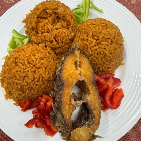 Three mounds of jollof rice with a fried fish steak, red bell peppers, and green bell peppers.