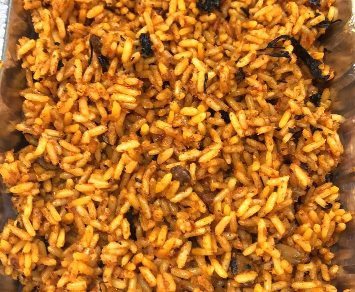 Close-up of a tray filled with spicy, orange-colored rice garnished with herbs and spices.