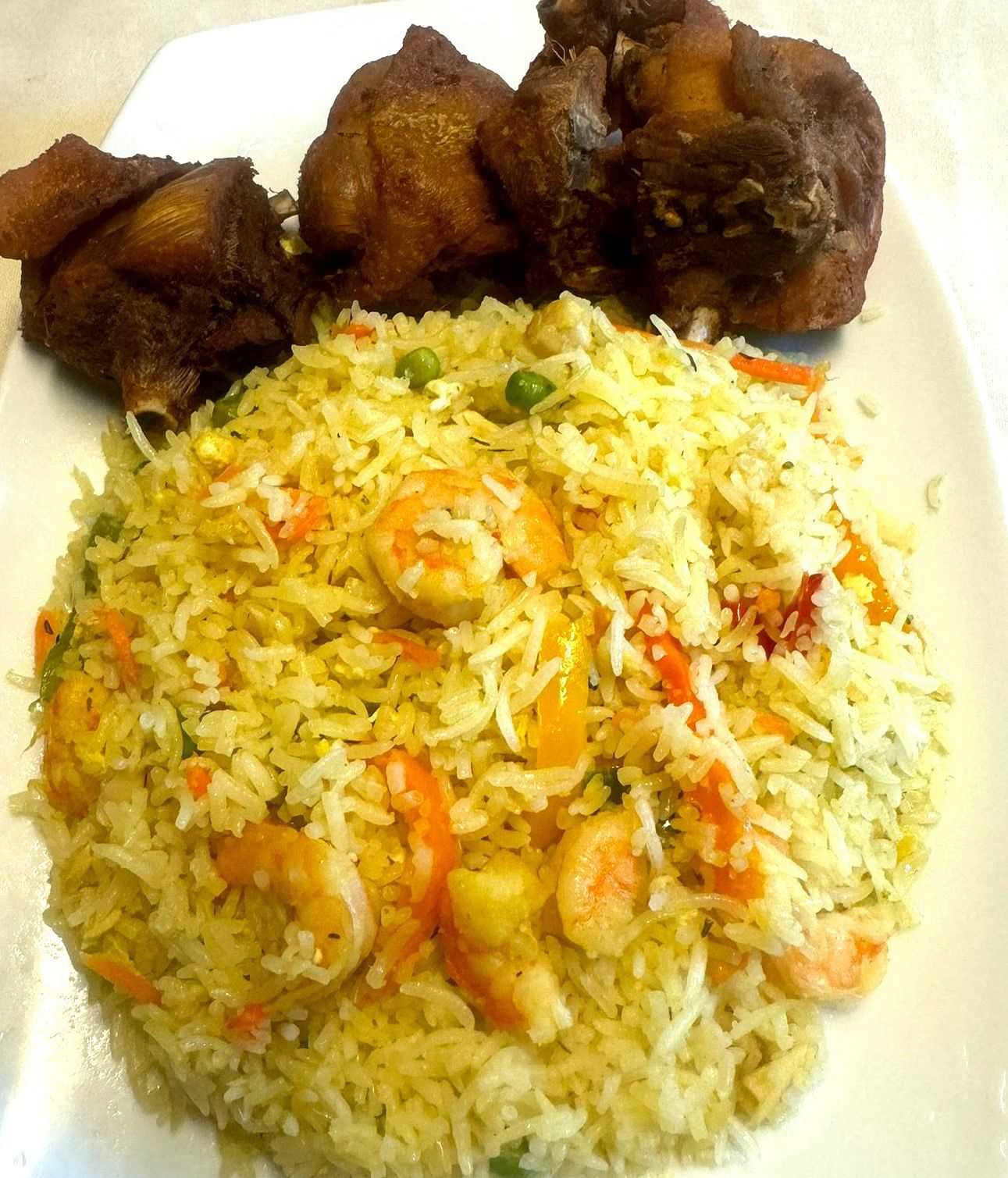 Fried rice with shrimp, peas, and carrots served with three pieces of fried chicken.