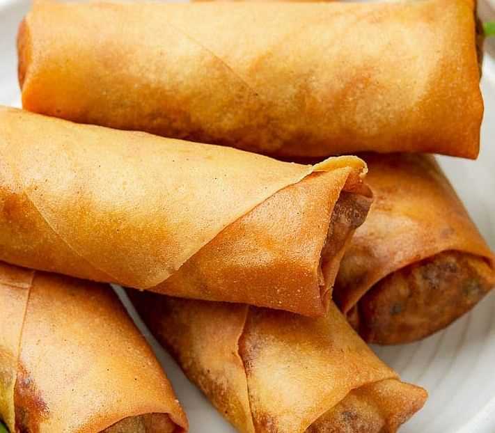 Four crispy, golden spring rolls on a white plate, ready to be served.