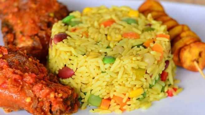 A plate of jollof rice with vegetables, grilled chicken, and fried plantains.